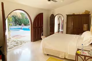 Sun-lit bedroom with arched doorways opening to the pool