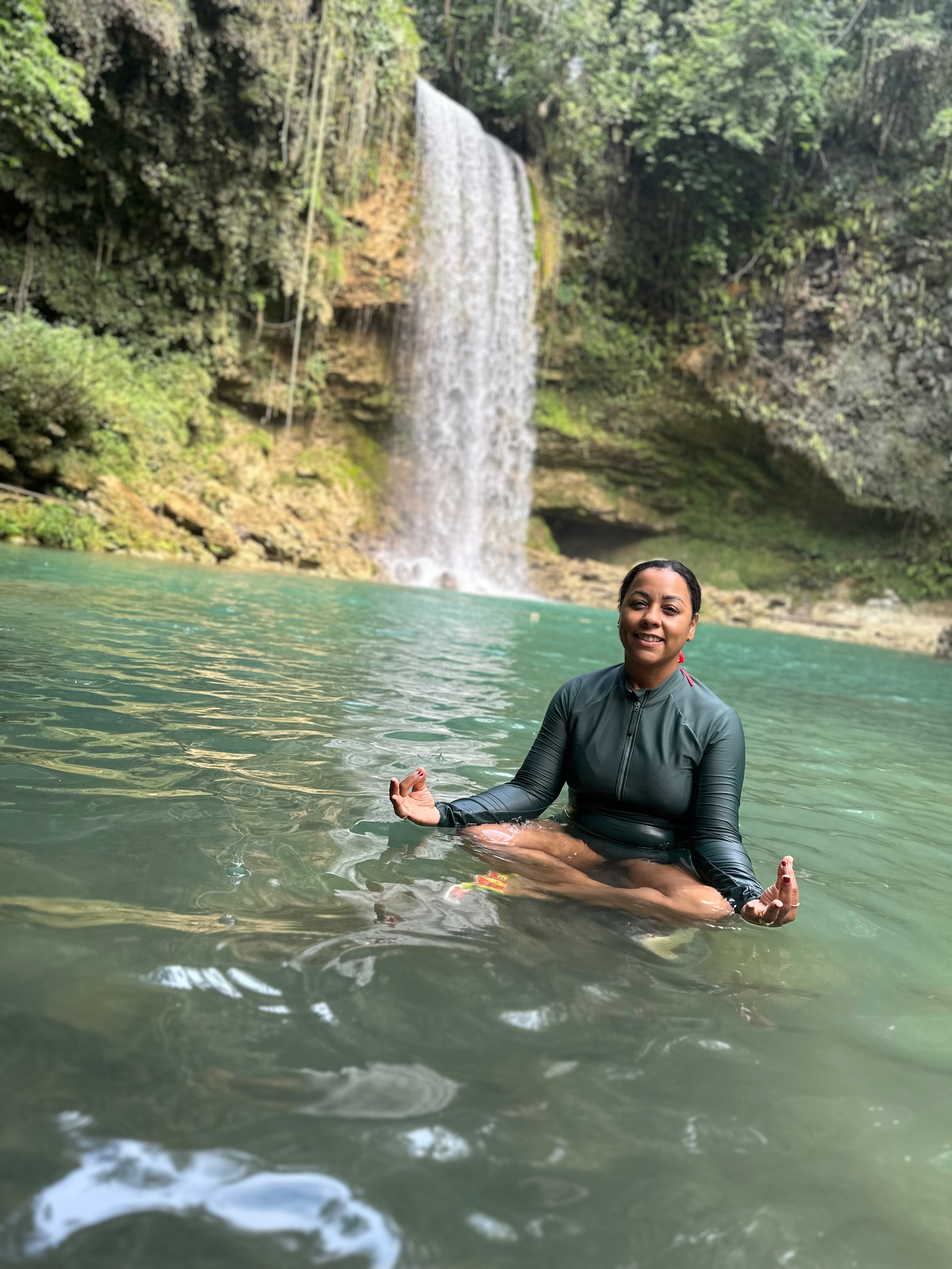 A guest meditates in turquoise waters beneath a cascading waterfall